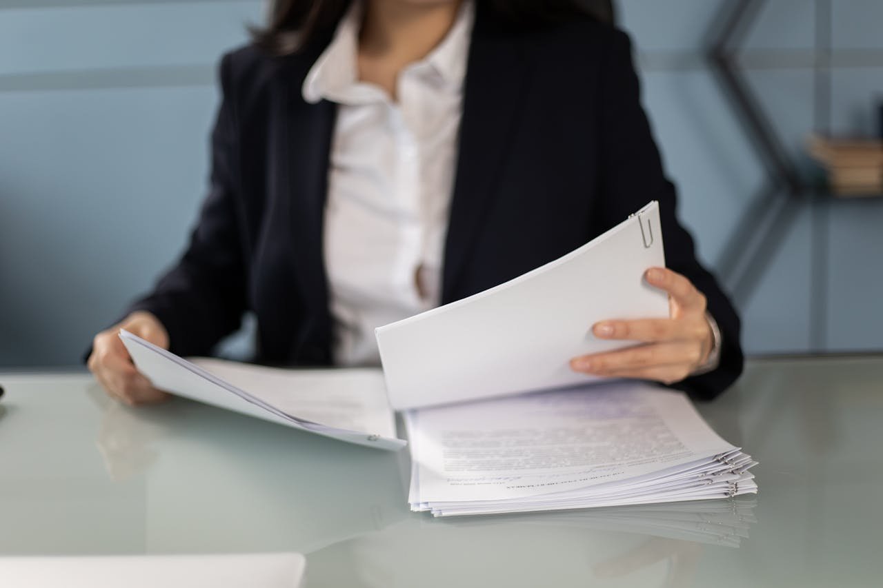 Businesswoman in formal attire reviewing and organizing documents at an office desk.
